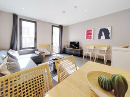 A modern living room with a sofa, dining table, chairs, a TV, and artwork on the wall.