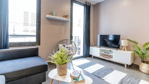 A modern living room with a sofa, a TV, a plant, and a bookshelf. - Bo&Co Apartments Sitges (Sitges)