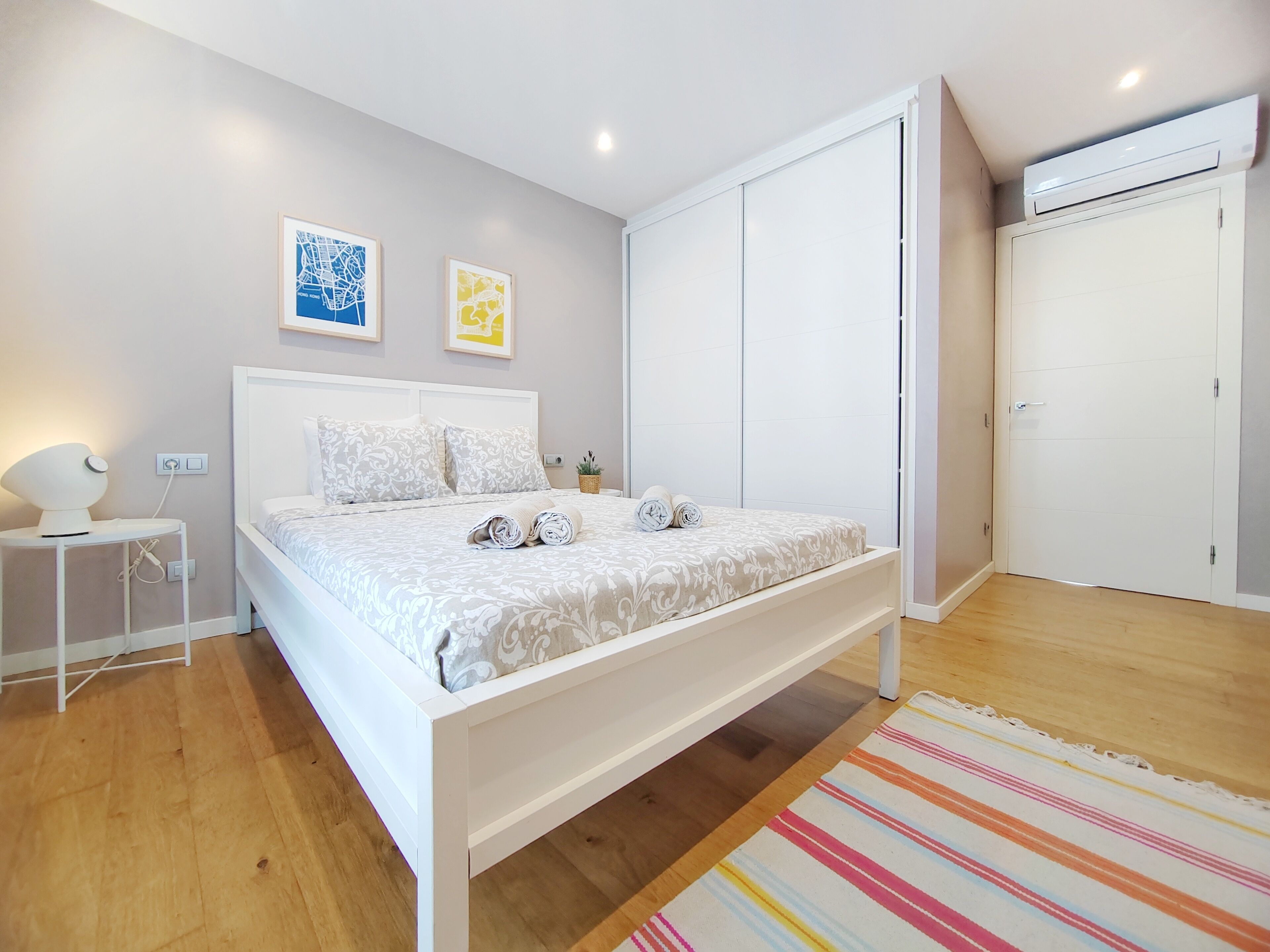 Un dormitorio ordenado con cama, mesitas de noche, aire acondicionado de pared y una puerta.