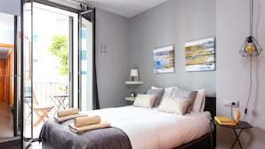 A modern bedroom with a bed, a nightstand, a wall-mounted lamp, and a small table with a book and a decorative item. - Bo&Co Apartments Sitges (Sitges)