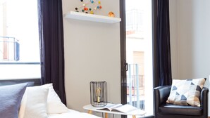 A modern hotel room with a bed, a reading chair, a small table with a book, and a view of the outside balcony. - Bo&Co Apartments Sitges (Sitges)
