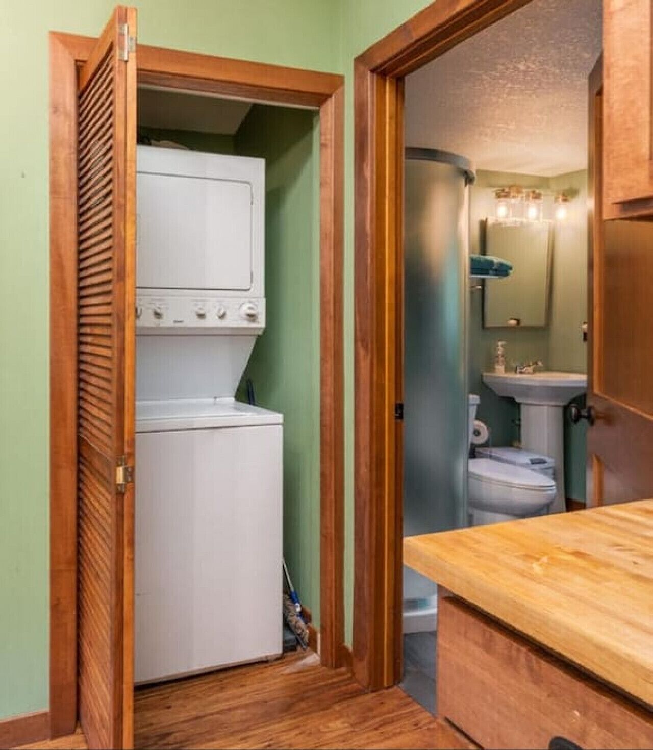 Une buanderie équipée d’un lave-linge et d’un sèche-linge, d’un banc en bois et d’un petit lavabo dans la salle de bain attenante.