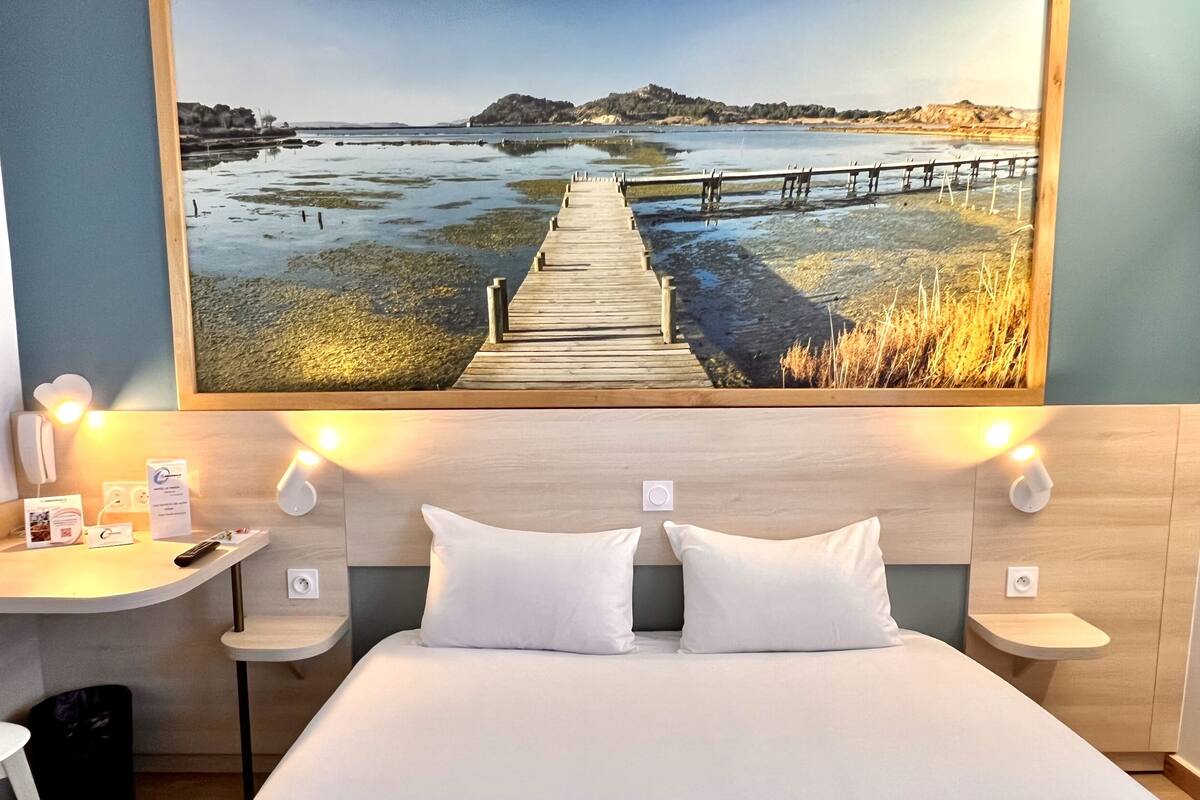 A hotel room with a large bed, two bedside tables, a desk, and a painting of a coastal landscape.