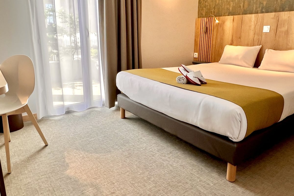A hotel room with a bed, a chair, and a view of the outdoors.