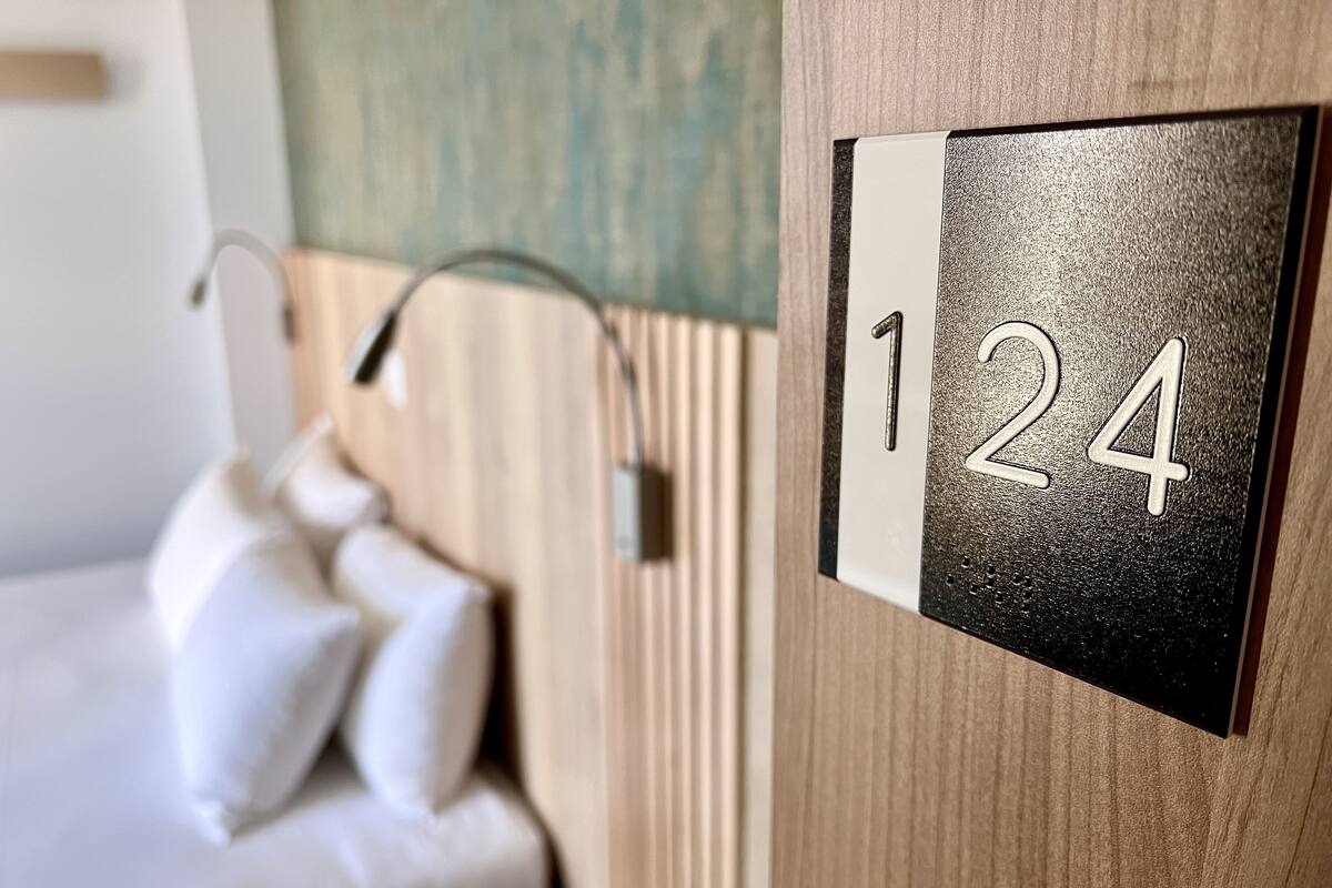 A hotel room with a bed, a nightstand, and a wall-mounted number plate displaying '124'.