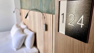 Habitación de hotel con cama, mesita de noche y placa con el número 124 colgada en la pared.