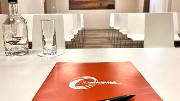 A hotel room with a table set for two, a bottle of water, a glass, and a red folder with the hotel logo.