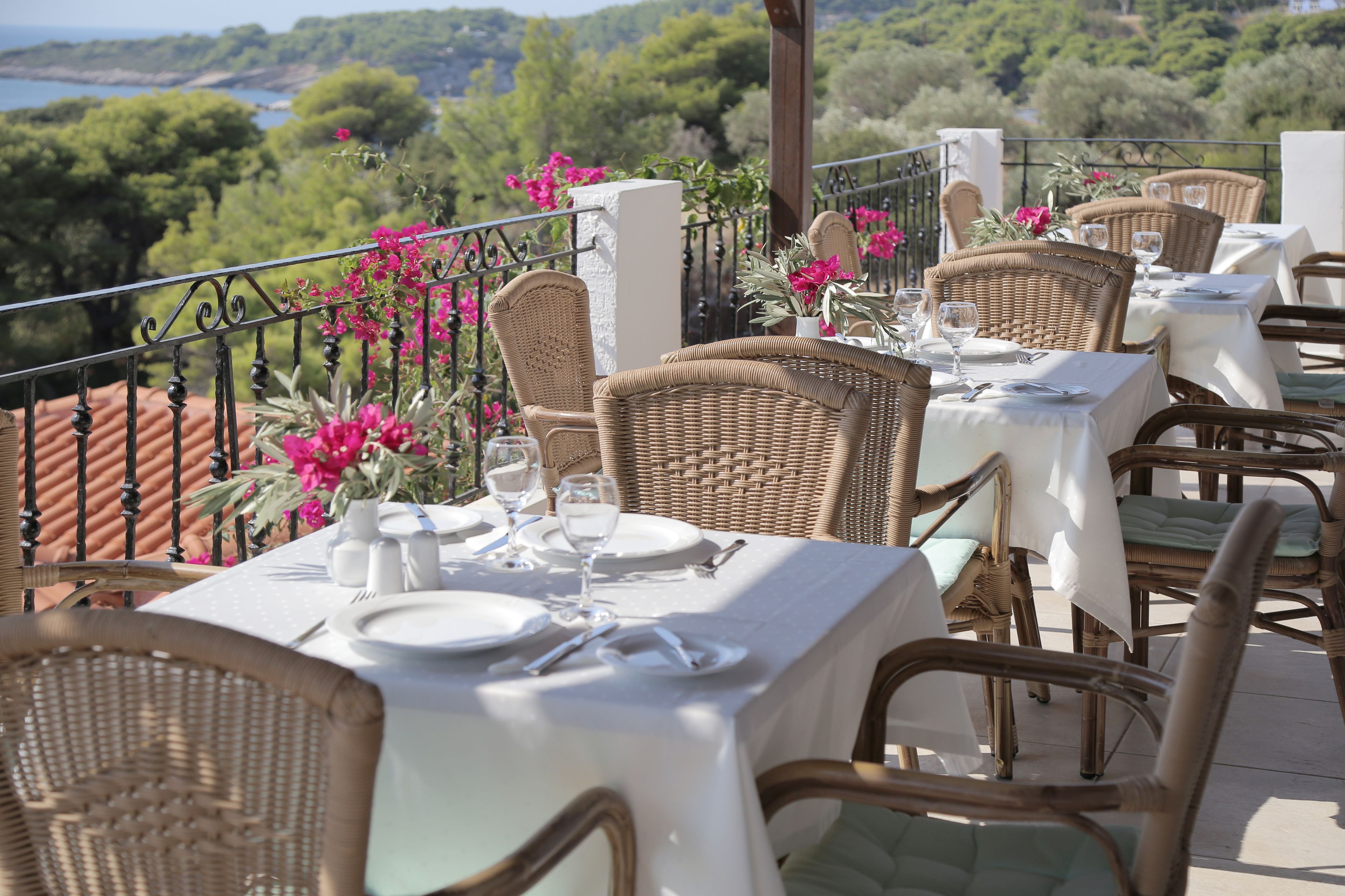 A terrace with wicker tables set for dining, overlooking a scenic landscape.