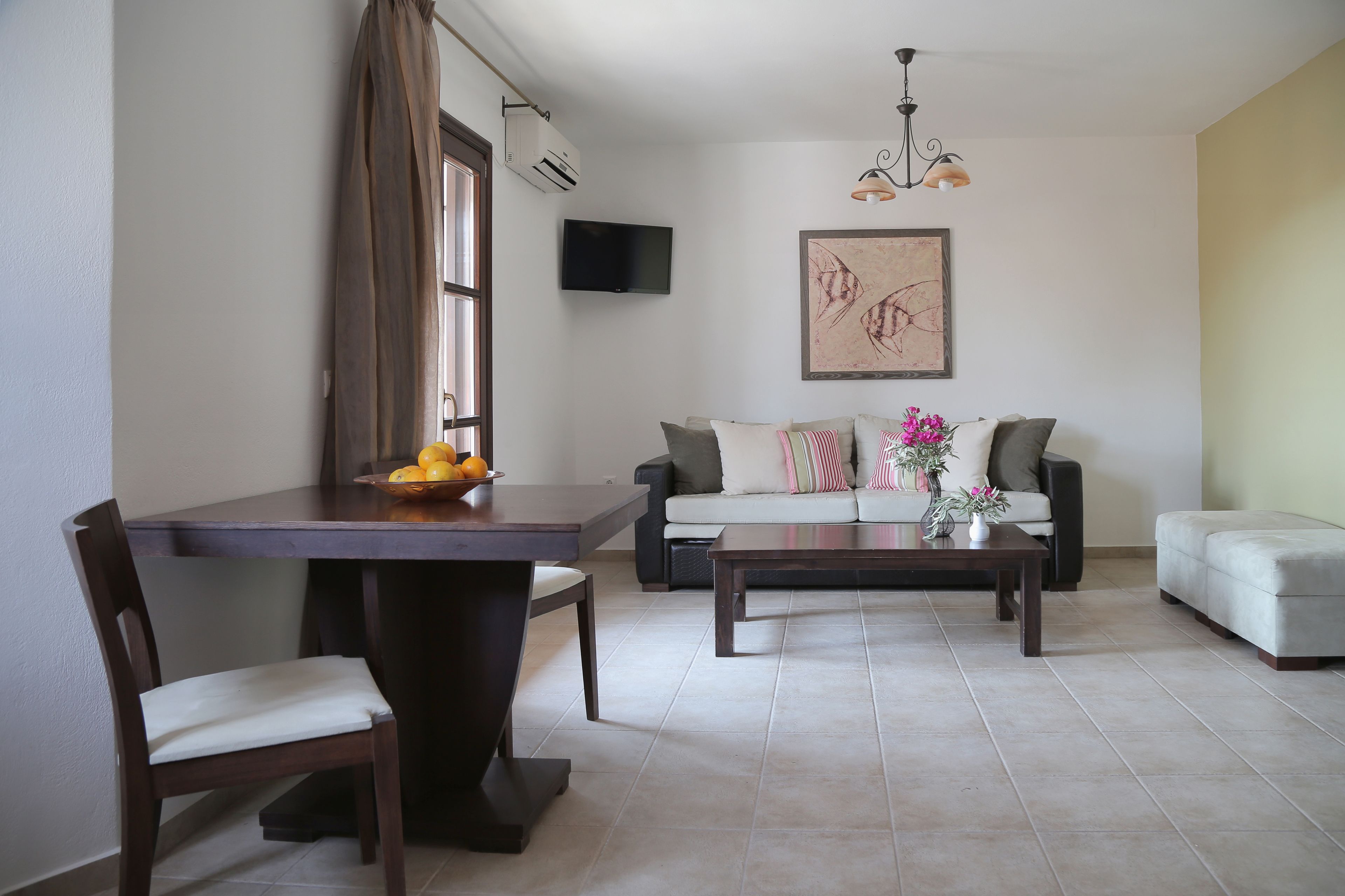 Un salon comprenant un canapé, une table basse, une table à manger avec des chaises, et un téléviseur à écran plat fixé au mur.
