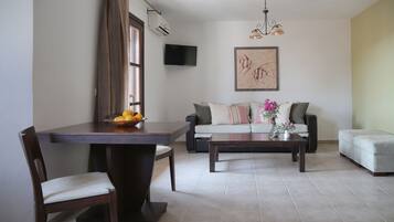 Un salon comprenant un canapé, une table basse, une table à manger avec des chaises, et un téléviseur à écran plat fixé au mur.