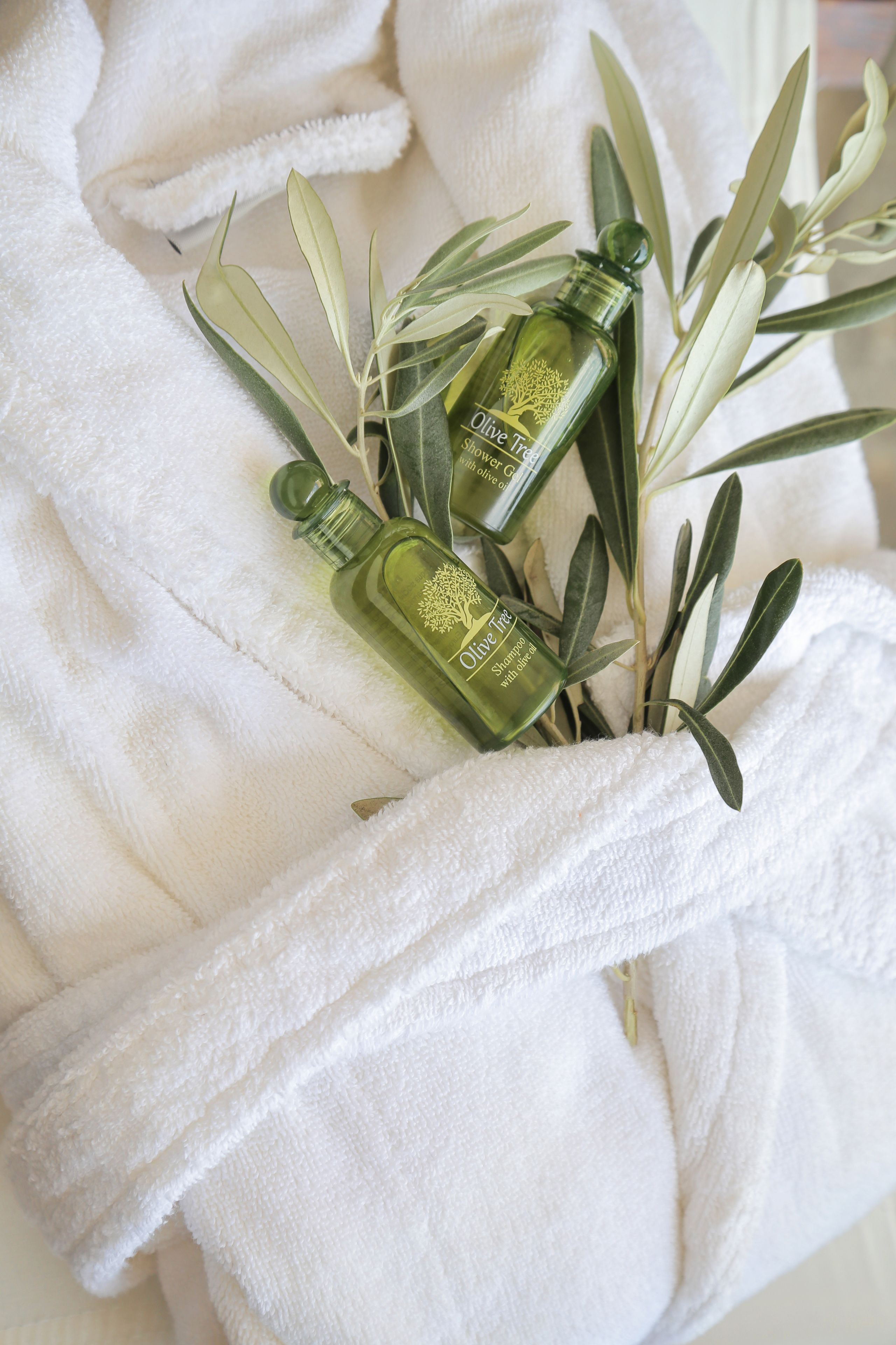 A white towel with two bottles of olive oil and green leaves.