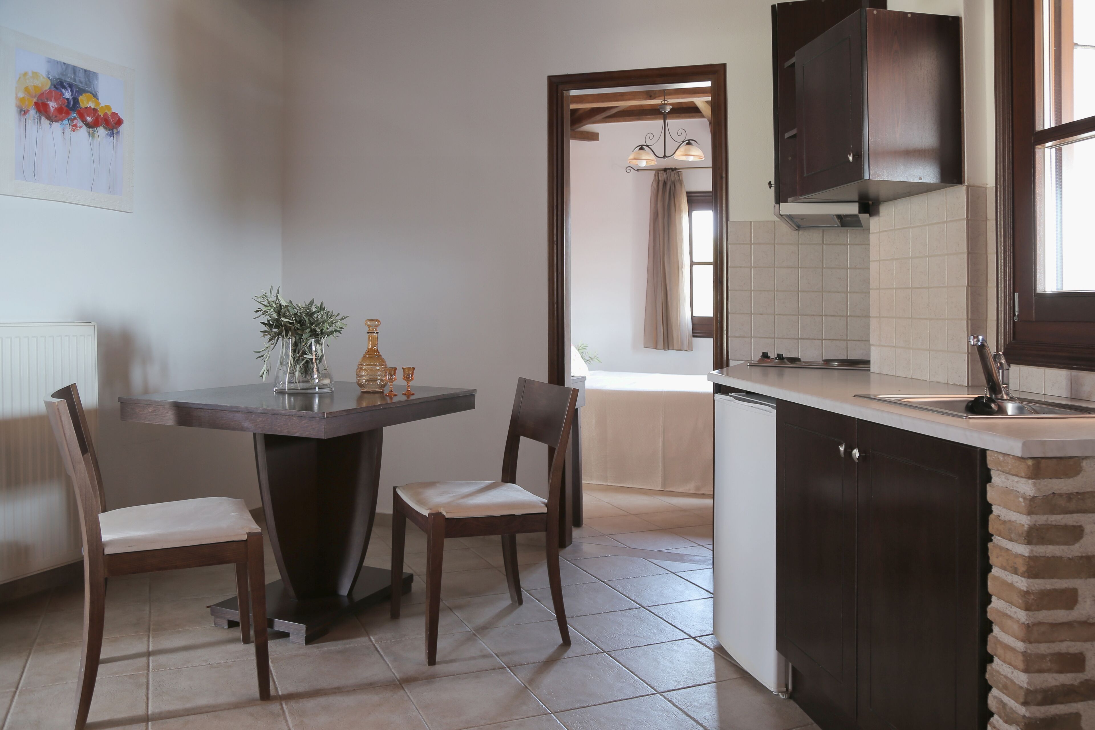 Una cucina con mobili impiallacciati in legno scuro, zoccolo paraschizzi rivestito in piastrelle e zona pranzo con tavolo e sedie.