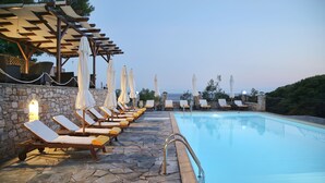 A poolside area with lounge chairs and umbrellas, a stone wall, and a clear view of the sea. - Yalis Hotel (Alonissos)