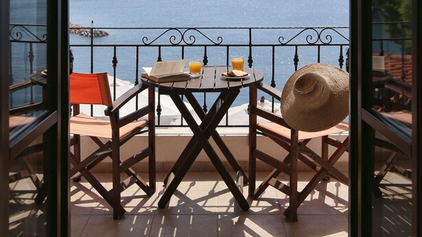 A balcony with a table, chairs, and a straw hat. - Yalis Hotel (Alonissos)
