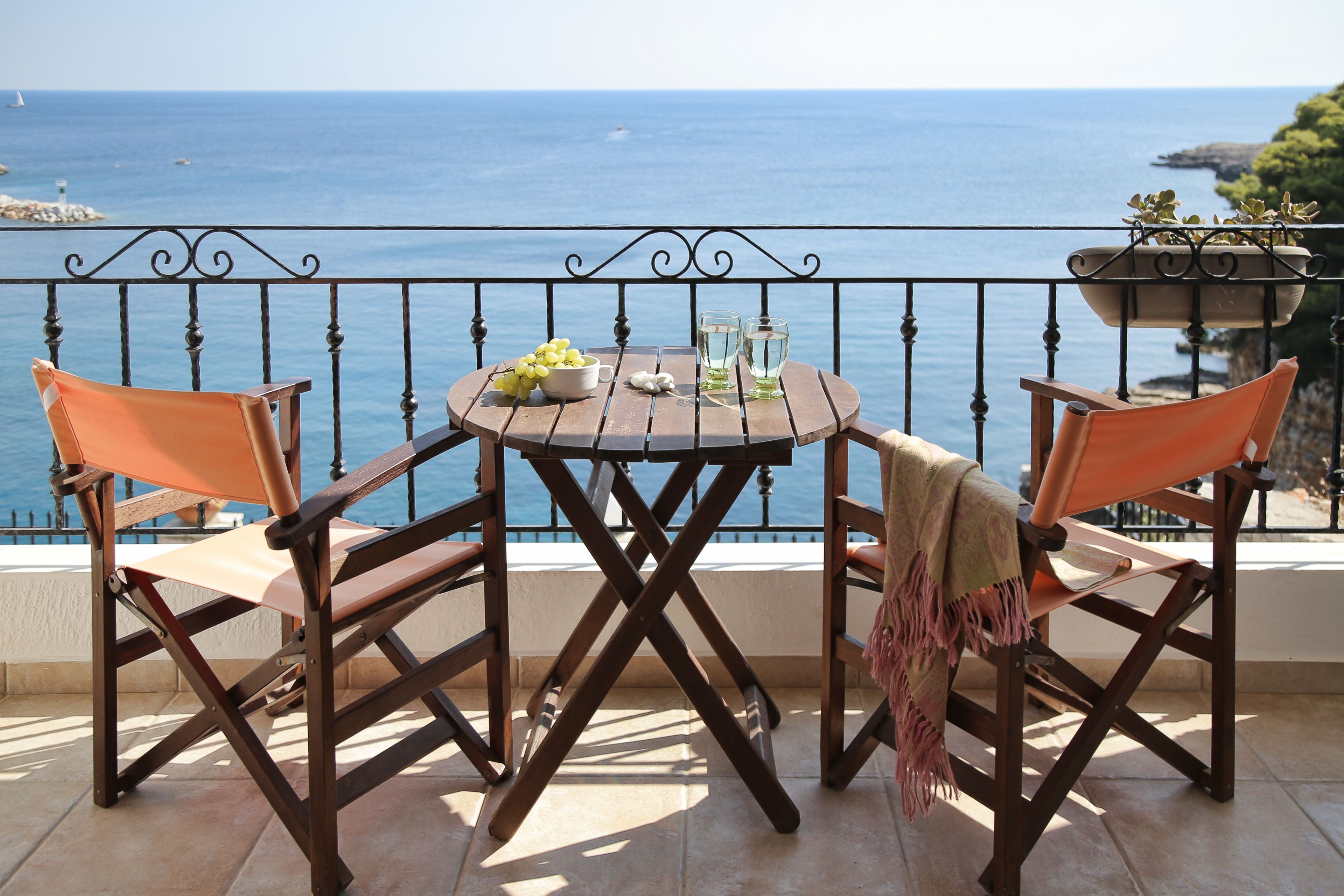A balcony with a table and chairs, overlooking the sea.