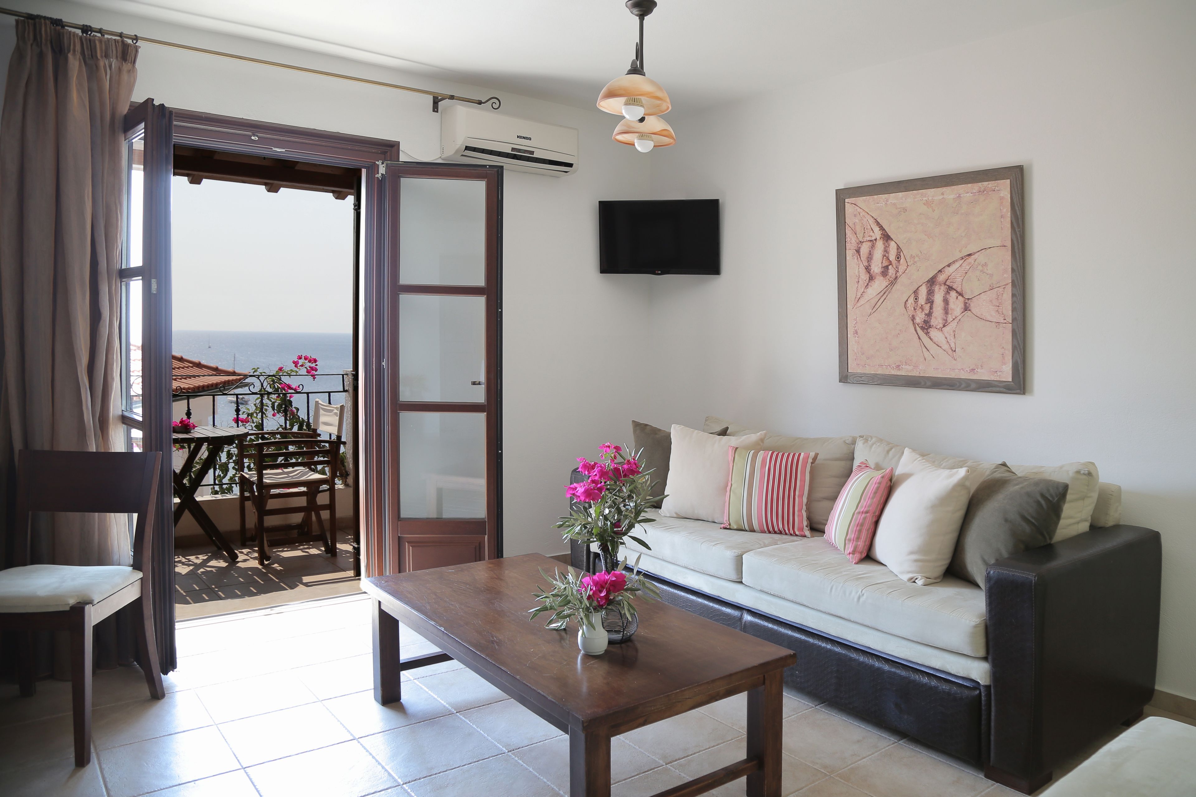 Una sala de estar con un sofá, una mesa de centro, un televisor y un balcón con mesa y sillas.