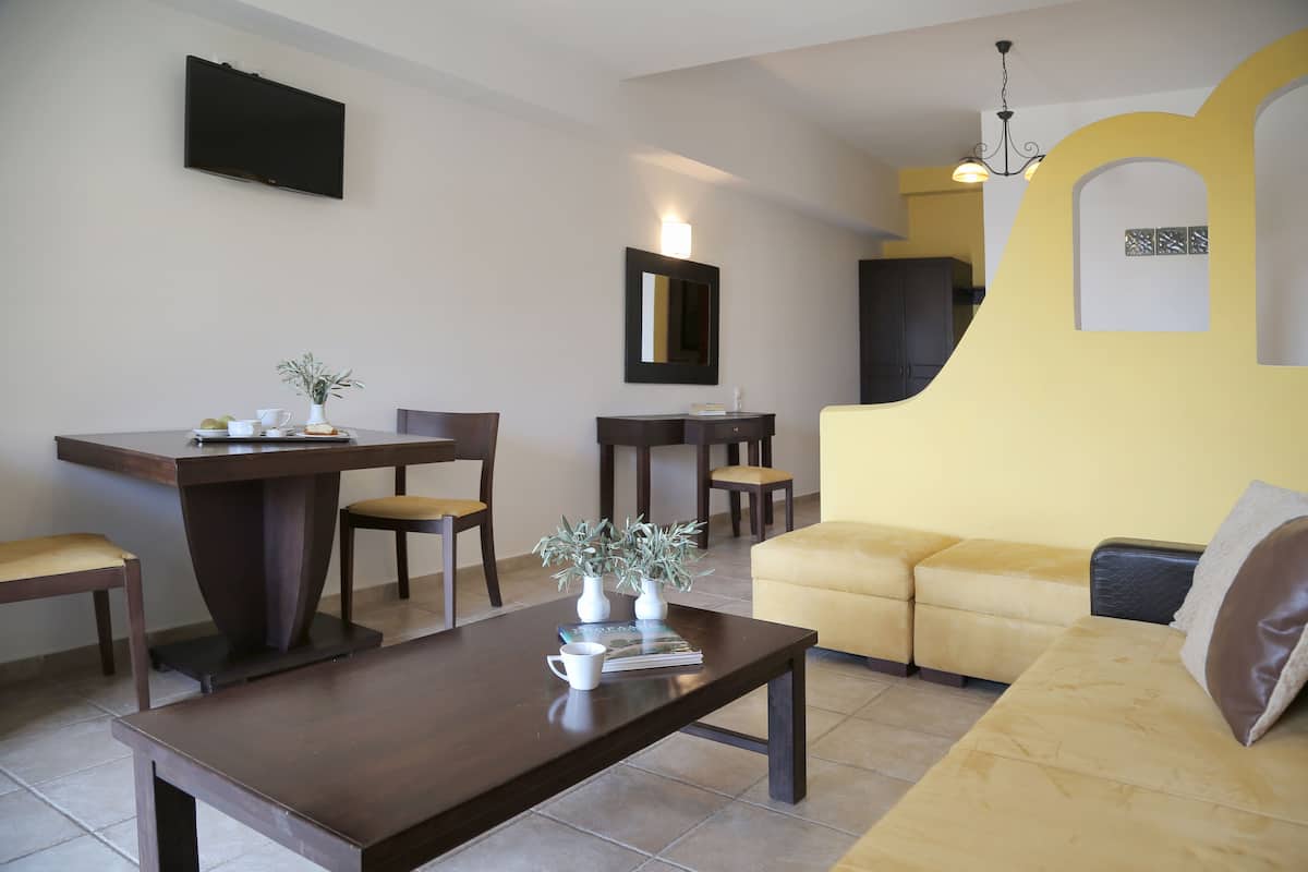 A living room with a sofa, a coffee table, a dining table with chairs, and a TV mounted on the wall.