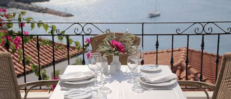 A table set for two with a view of the sea and a cliff.