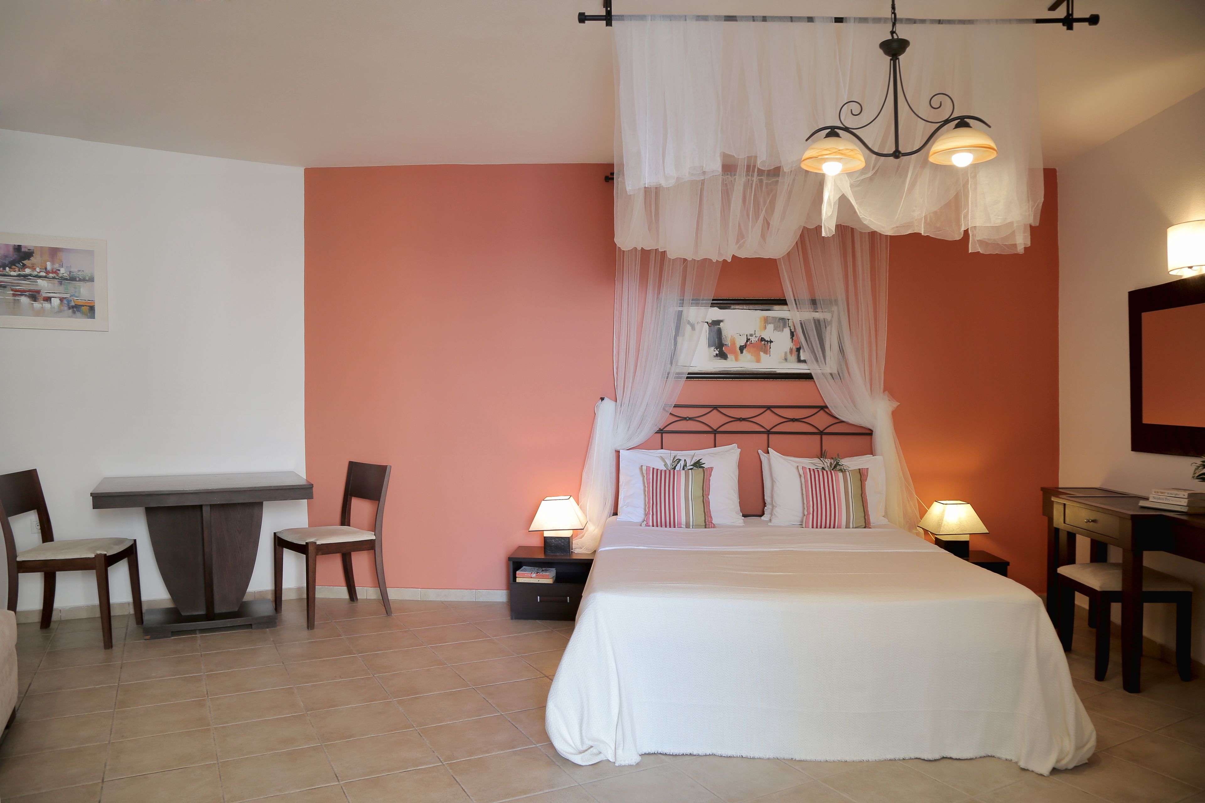 A bedroom with a bed, two bedside tables with lamps, a chair, a desk, and a picture on the wall.