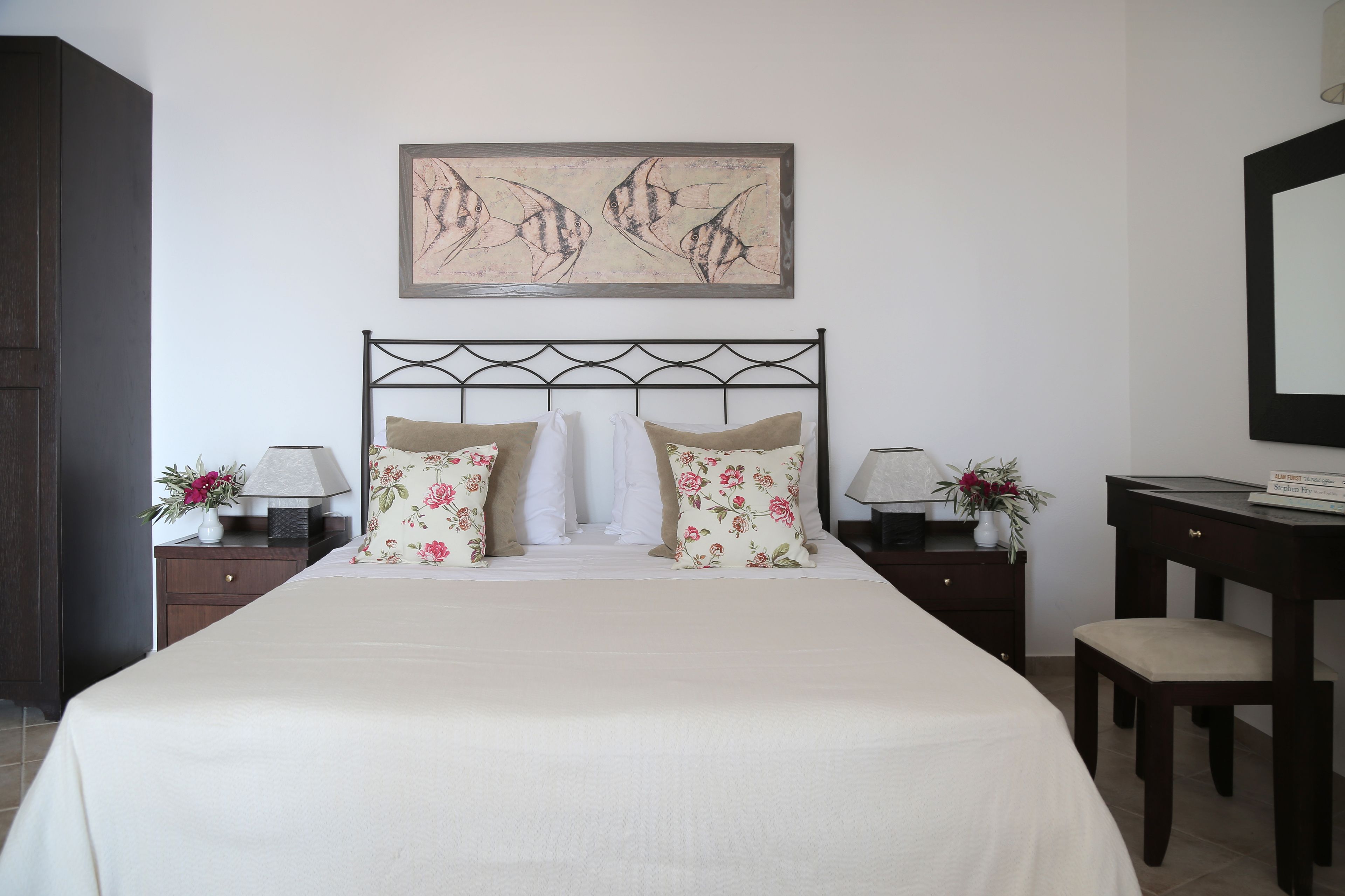 A neatly made bed with floral pillows, a headboard with a decorative pattern, and a wall-mounted artwork above it.