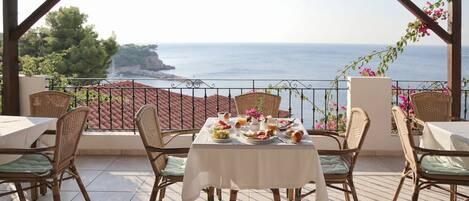 Eine Terrasse mit Korbstühlen und einem Tisch, gedeckt für das Frühstück, mit Blick aufs Meer.