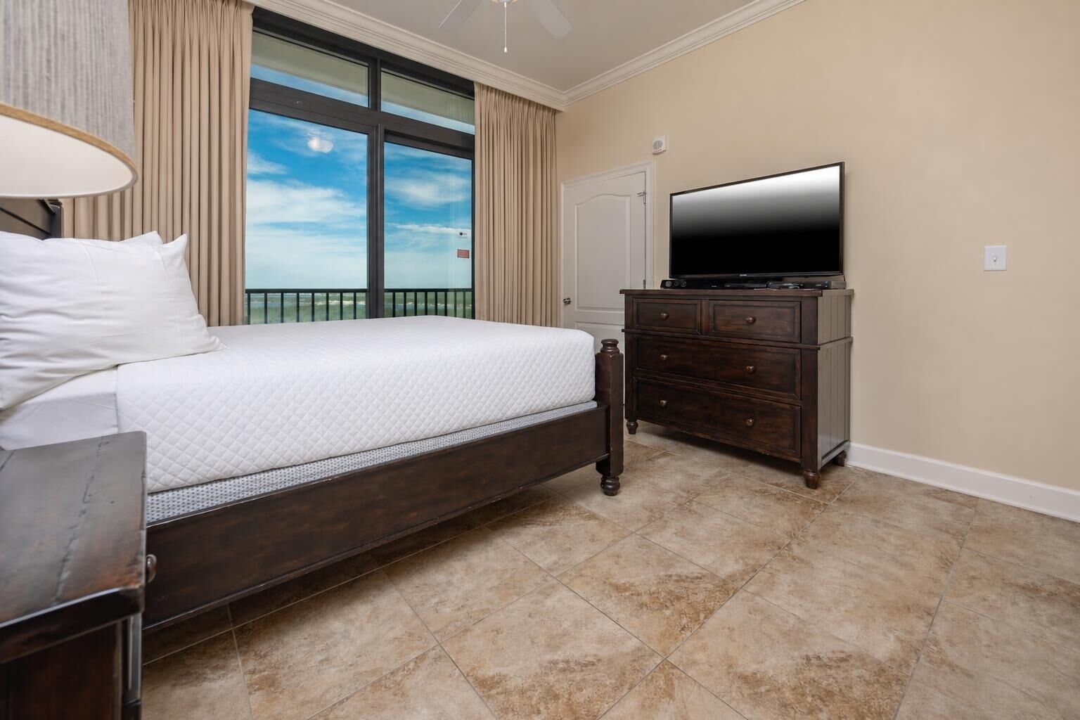 Une chambre à coucher avec un lit, une commode, un téléviseur et une fenêtre avec des rideaux.