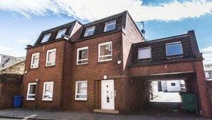 A two-story brick building with multiple windows, a garage, and a visible trash bin. - Mossie Apartment (Ayr)