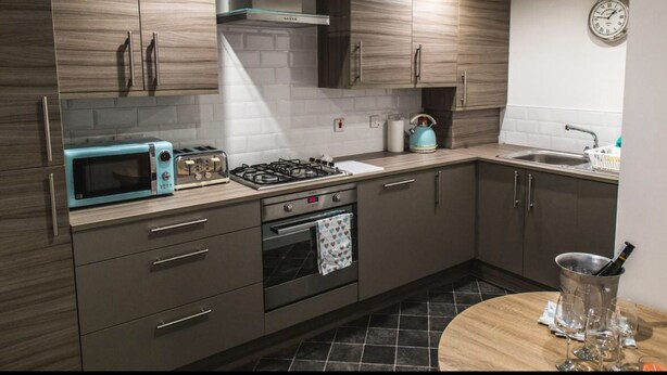 A modern kitchen with dark wood cabinets, a gas stove, a microwave, and a kettle. - Mossie Apartment (Ayr)