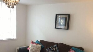 A living room with a brown sofa, two patterned throw pillows, a framed picture on the wall, and a hanging light fixture. - Mossie Apartment (Ayr)