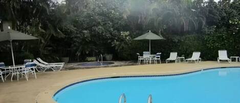 A swimming pool with lounge chairs and umbrellas, surrounded by dense foliage.