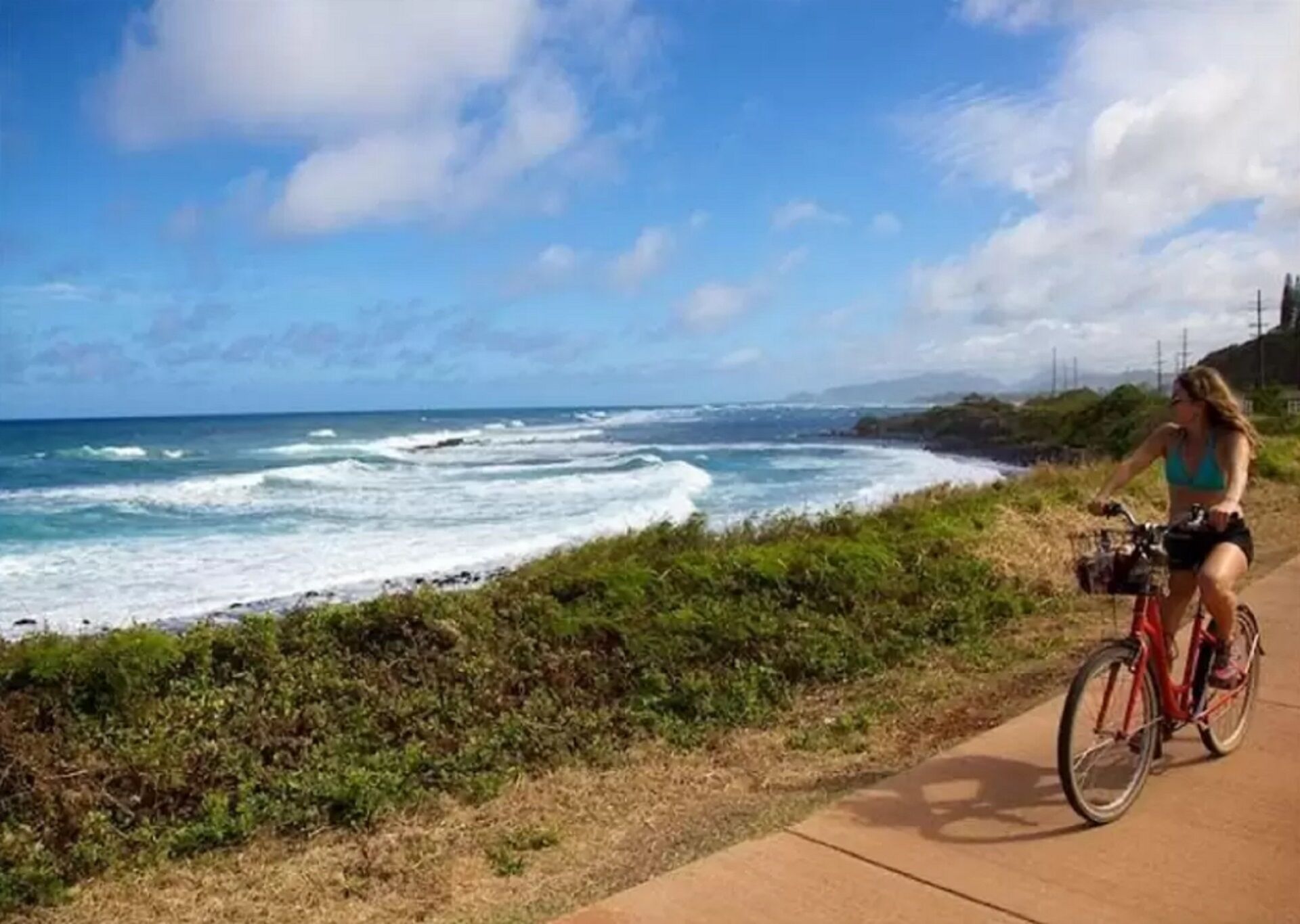 Une femme fait du vélo sur une piste cyclable le long de la côte, avec vue sur l’océan.