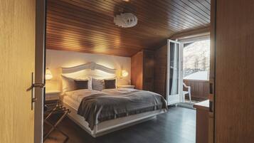 A modern bedroom with a wooden ceiling, a large bed with a headboard, bedside lamps, and a view of the outdoors through a glass door.
