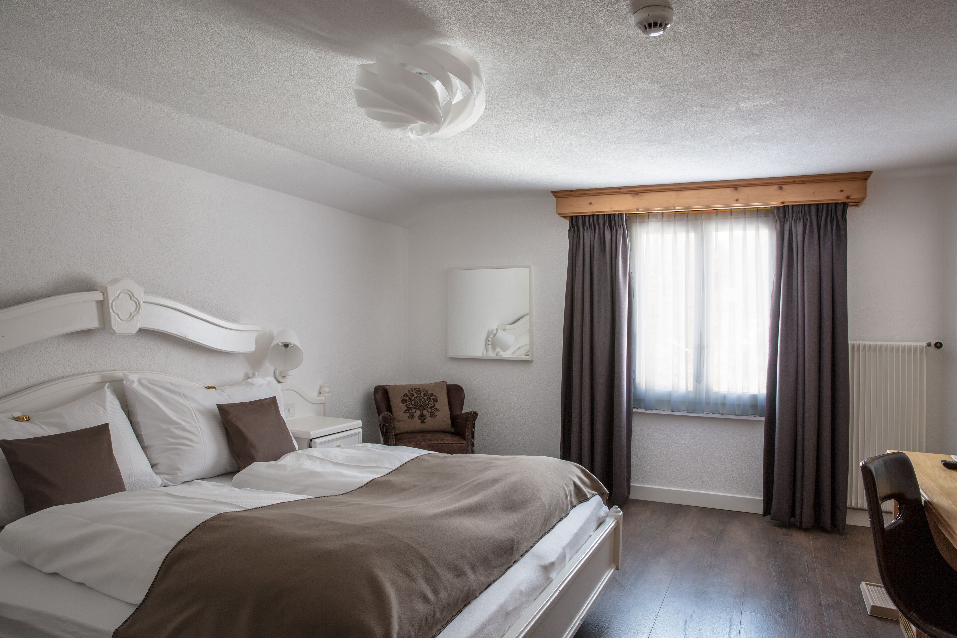 A bedroom with a large bed, a chair, a desk, and a window with curtains.
