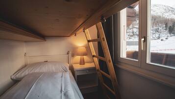 A small, cozy room with a bed, a nightstand, a lamp, and a window with a view of a snowy landscape.