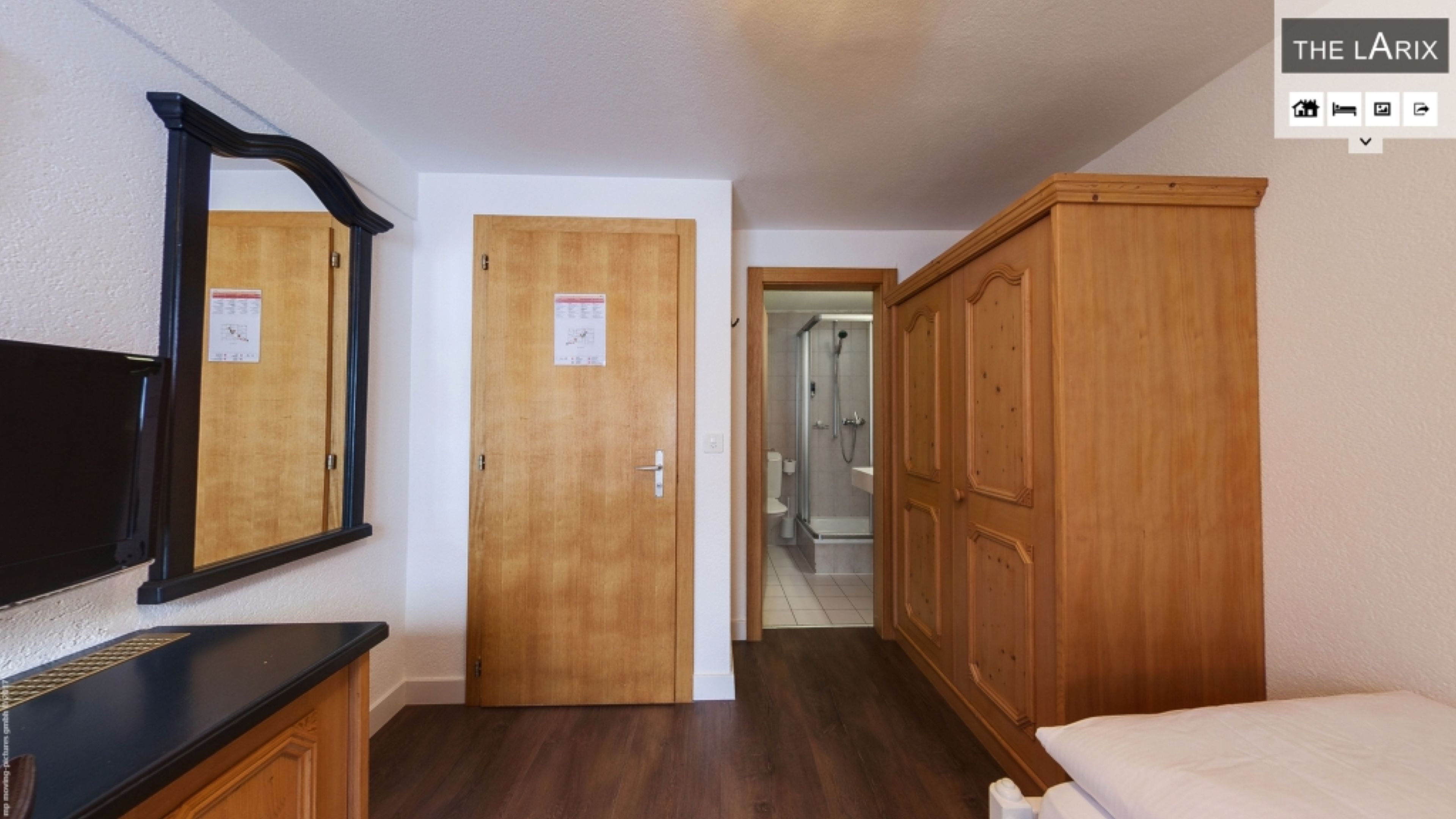 Una habitación de hotel con un armario de madera, un espejo y un televisor sobre un pedestal negro.