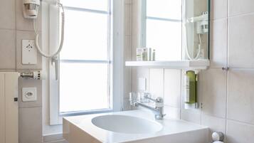 A modern bathroom with a large sink, a mirror, a towel rack, and a window.