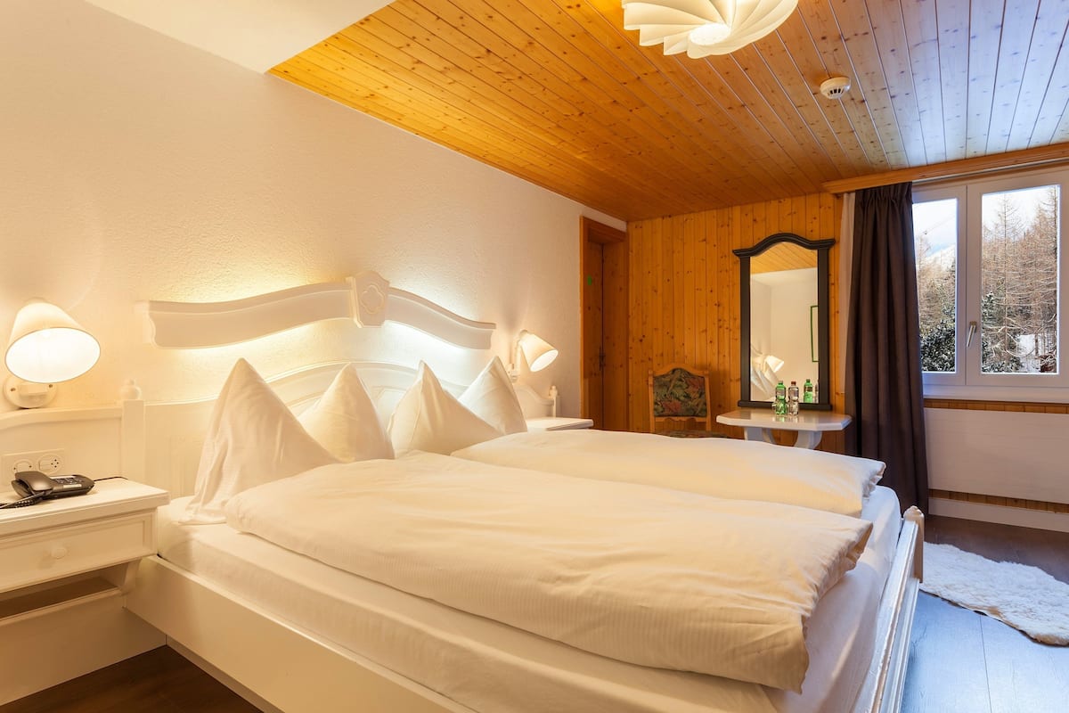 A double bed with white bedding, a bedside table with a lamp, and a wooden ceiling.