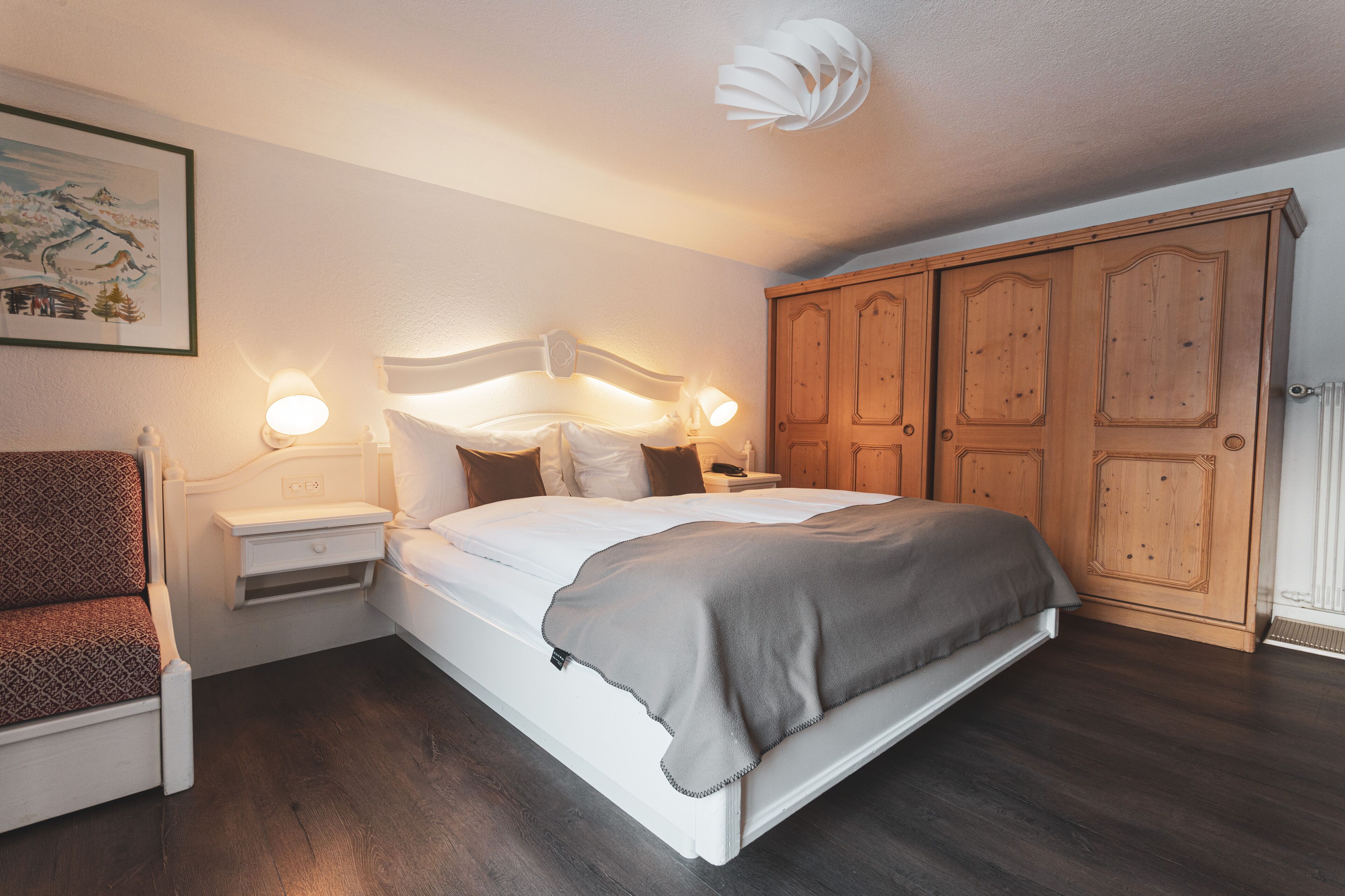 Un dormitorio con cama, mesitas de noche, una silla y un armario.