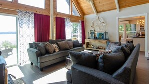 A spacious living area with a large sofa set, a wooden ceiling, and a view of the outdoors. - Island house located on Stretch Island close to Fair Harbor (Grapeview)