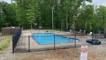 A fenced outdoor swimming pool with a basketball hoop and lounge chairs.