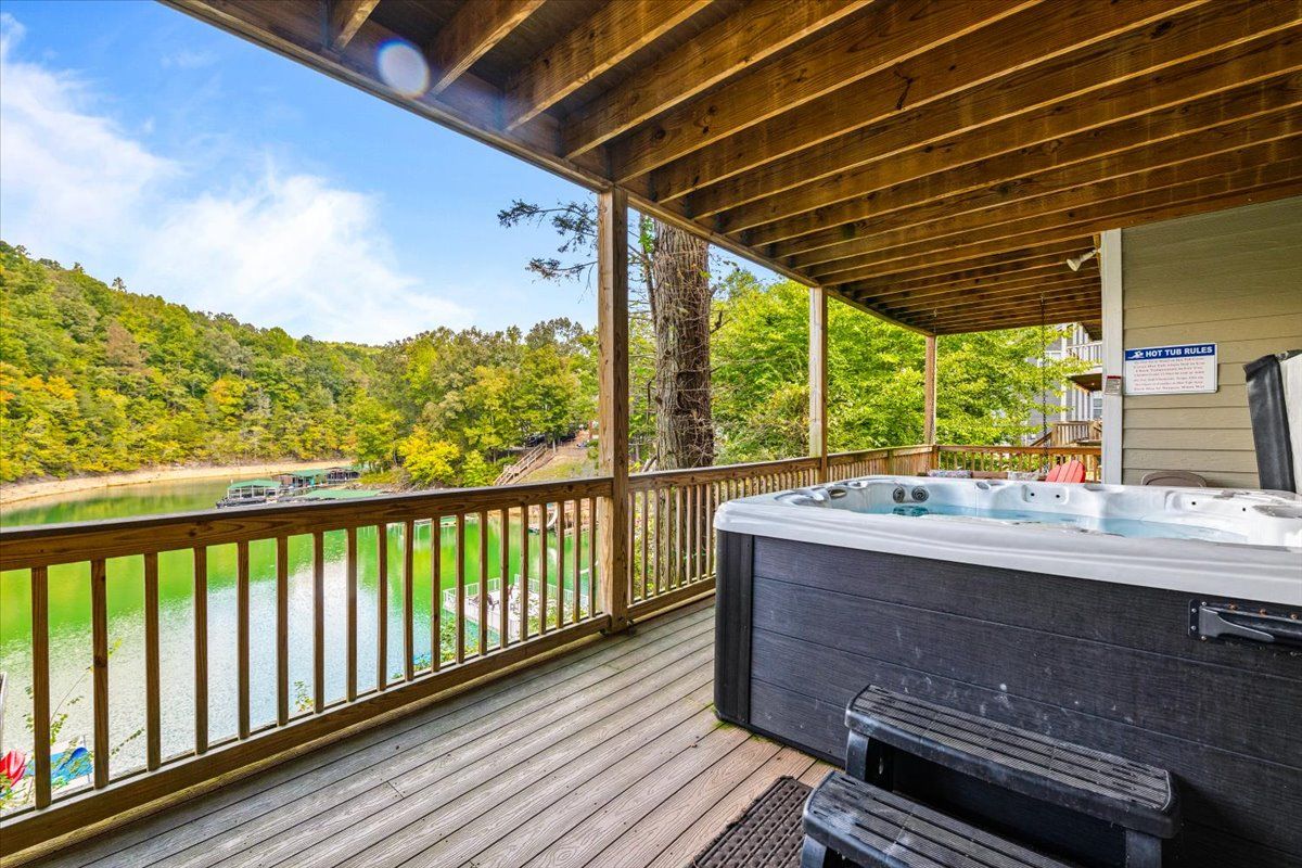Un bain à remous sur une terrasse en bois, avec vue sur un lac et une colline boisée.
