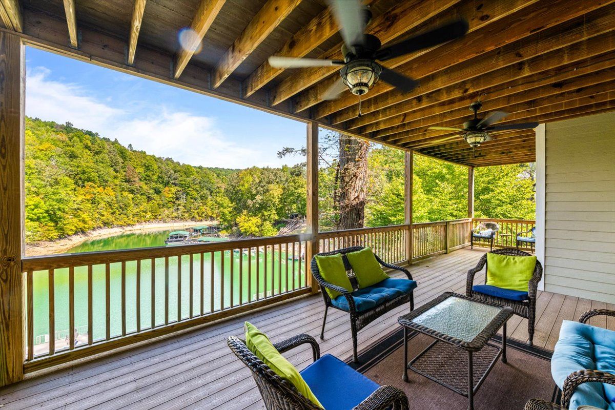 Une terrasse extérieure couverte, aménagée avec des meubles en osier, offrant une vue sur un lac et une colline boisée.
