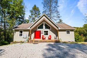A two-story house with a red front door, a covered porch with two chairs, and a gravel driveway. - Fall Special! 3+nights @ 15% off  | 9BR/9BA Private Dock + Hot Tub | Quiet Cove (LaFollette)