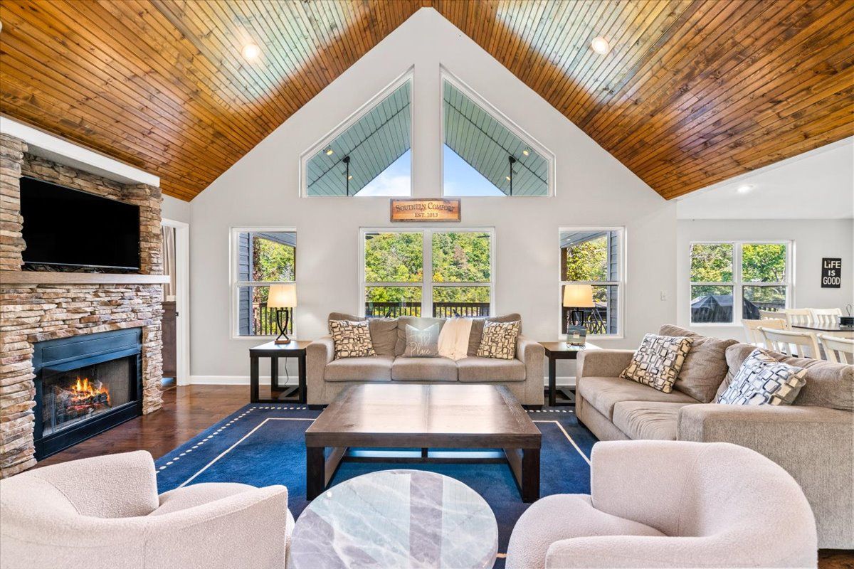A spacious living room with a stone fireplace, a large coffee table, and a high ceiling with wooden beams.