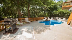 Un área de piscina al aire libre con una parrilla, sillas de descanso y una terraza de madera.