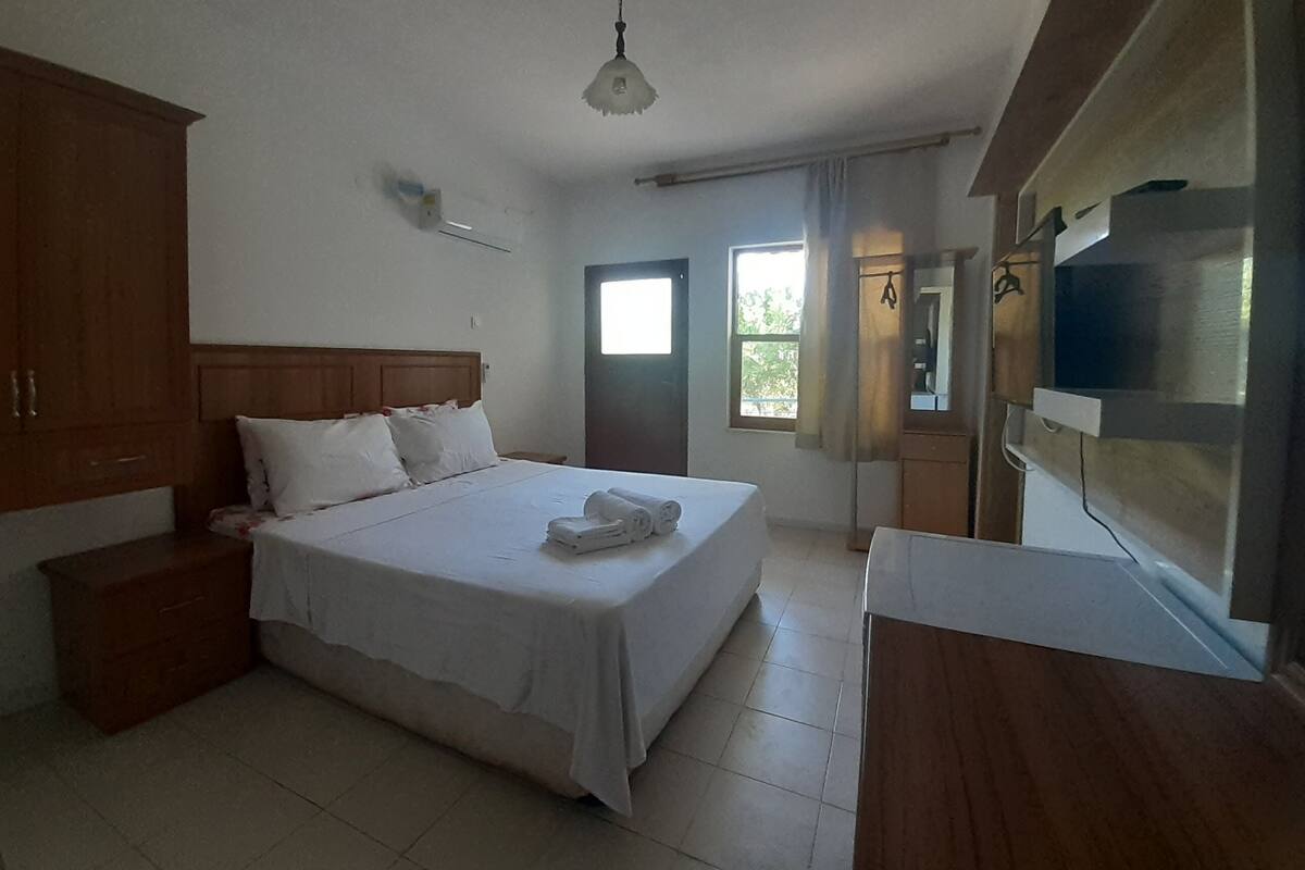 A bedroom with a bed, wooden wardrobe, bedside table, and a TV.