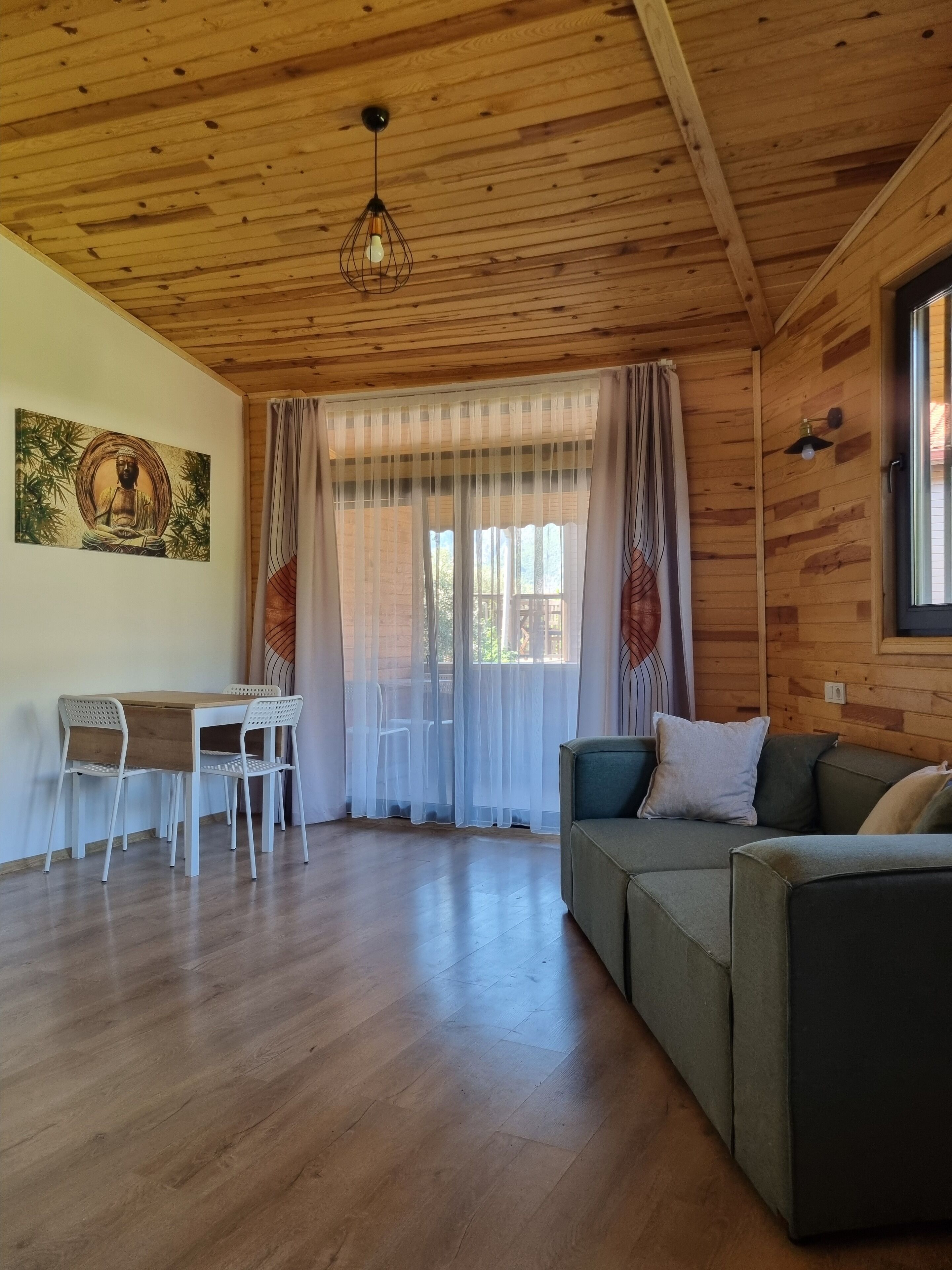 A wooden interior with a dining table and chairs, a sofa, and a painting on the wall.
