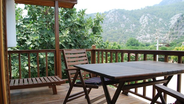 Un terrazzo in legno con tavolo e sedie, affacciato su un paesaggio montuoso.