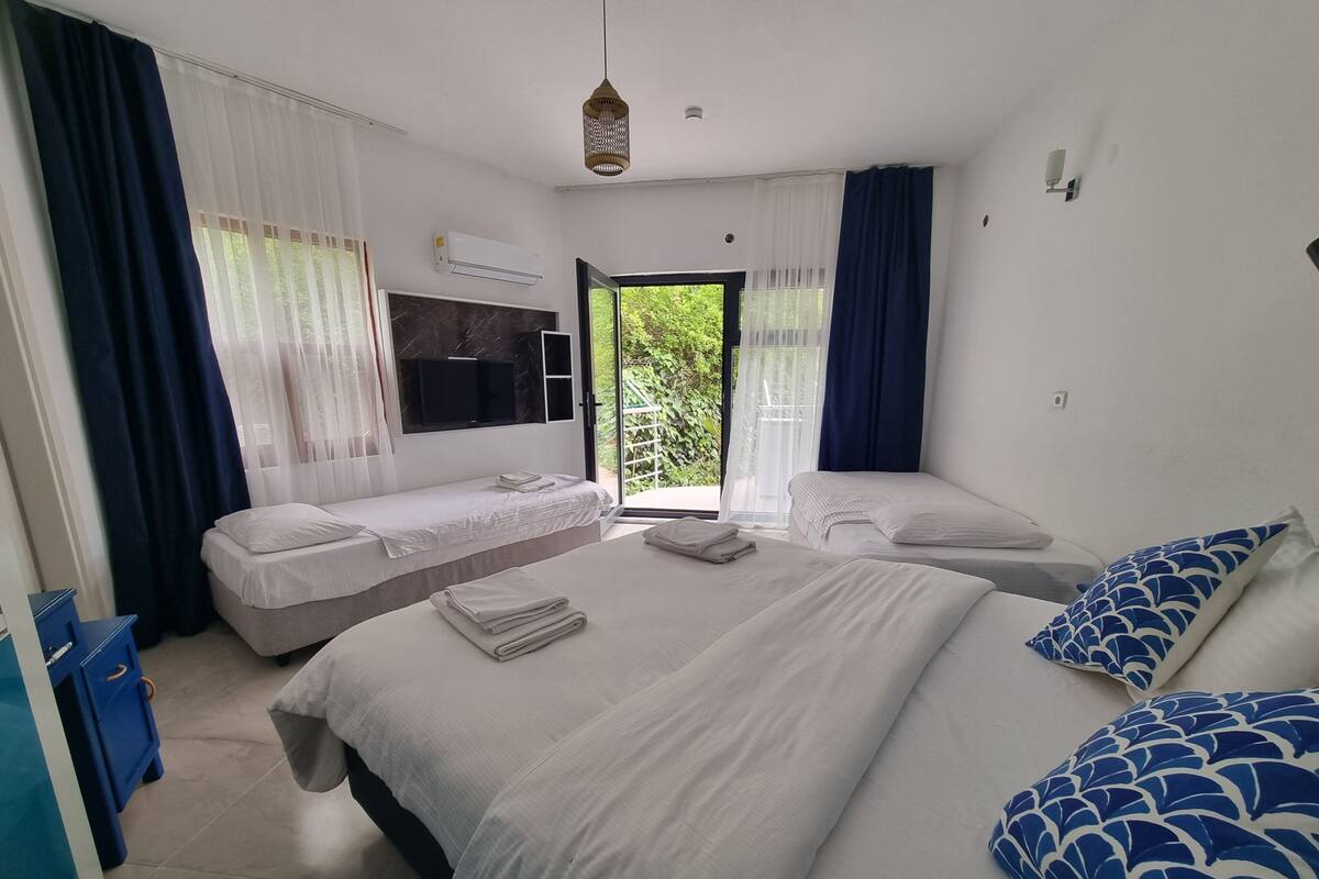 A hotel room with two beds, a TV, an air conditioning unit, and a view of greenery.
