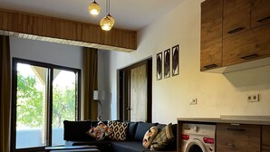 Un soggiorno moderno con divano, poggiapiedi e lavatrice. Sono presenti mobili contenitori in legno e una lampada a soffitto.